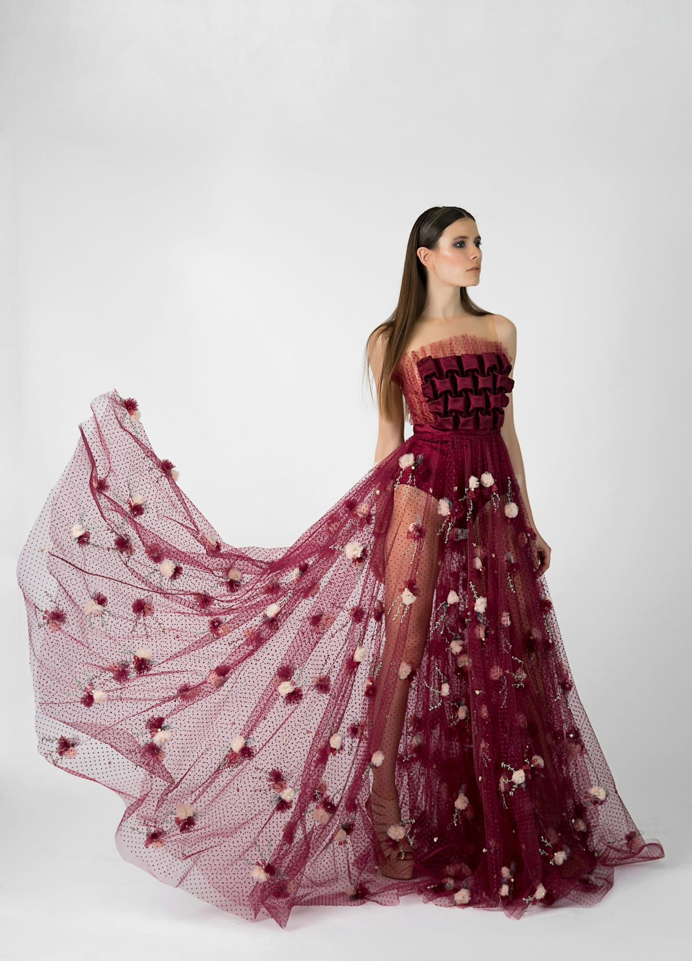 Woman in a strapless burgundy tulle gown with sculpted bodice and a sweeping floral train