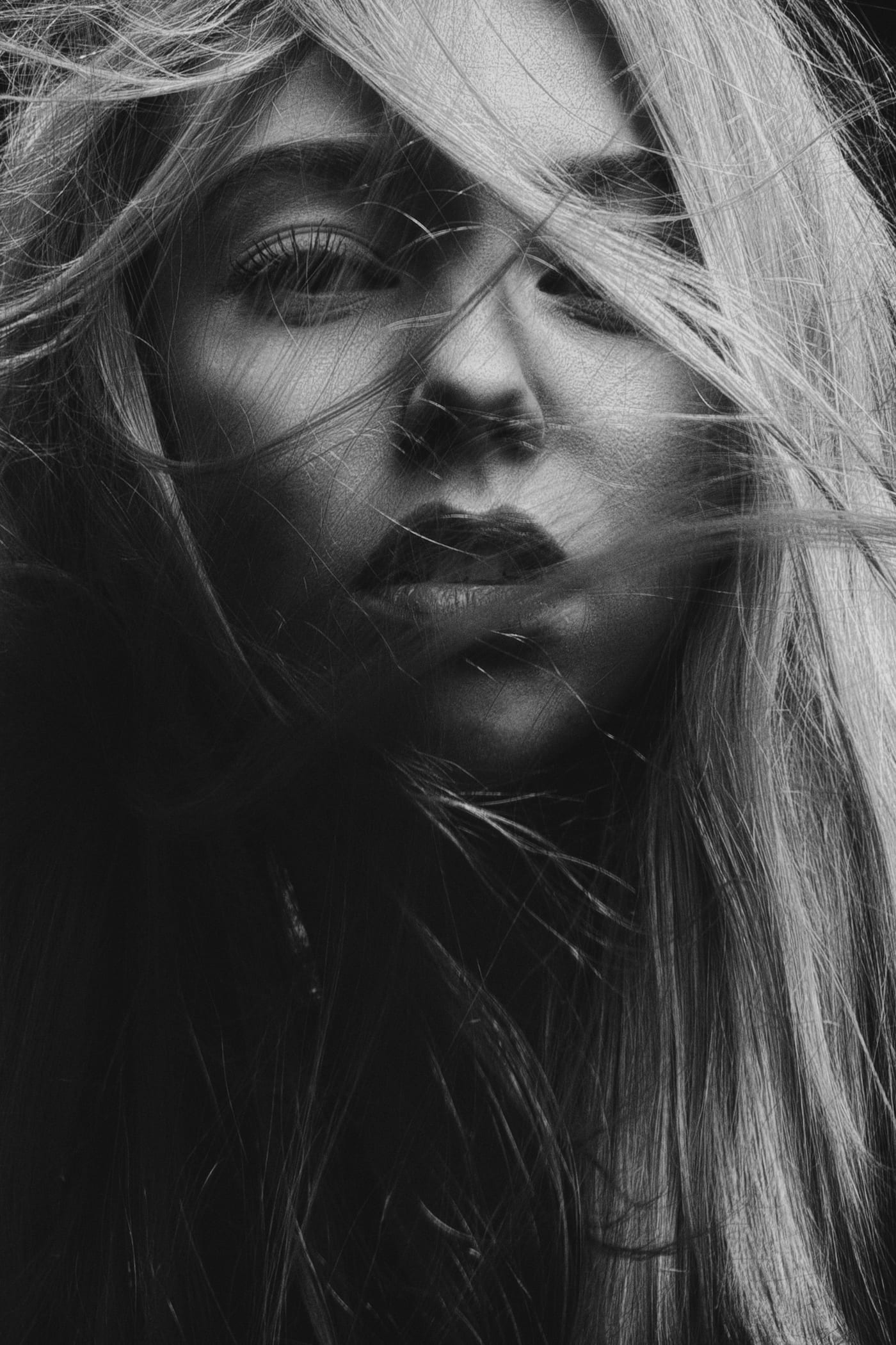 Black and white close portrait of a woman with long hair blowing across her face